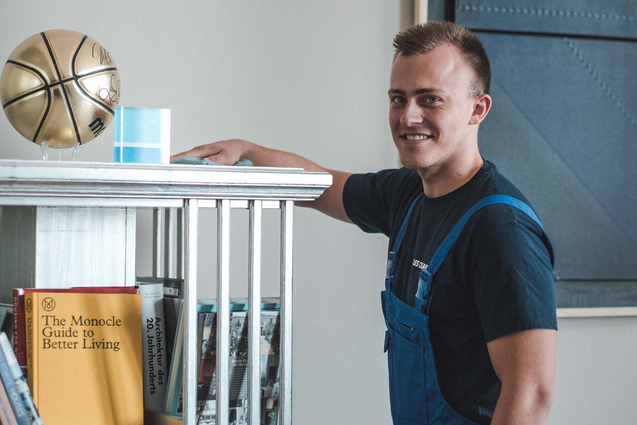 Büroreinigung Berlin Ein Mitarbeiter unserer Reinigungsfirma putz ein Regal in einem Büro in Berlin.