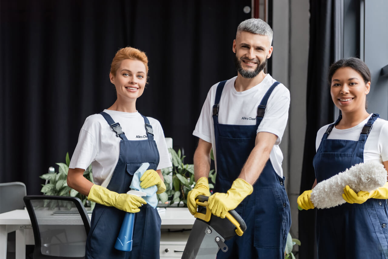 Ihre Reinigungsfirma in Berlin 3 Personen, 1 Mann und 2 Frauen, Mitarbeiter von Alles-Clean24 in Arbeitskleidung, posieren mit Arbeitsmitteln der Reinigungsfirma.