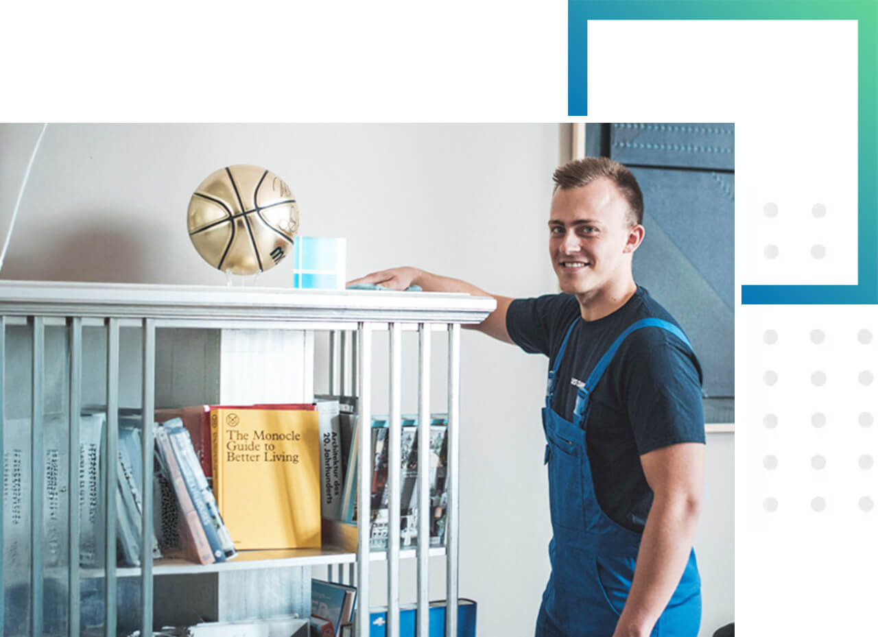 Wir halten individuelle Reinigungslösungen für Ihr Unternehmen bereit. Ein Mitarbeiter in Arbeitssachen putzt ein Regal in einm Büro - individuelle Reinigungslösungen für Ihr Unternehmen