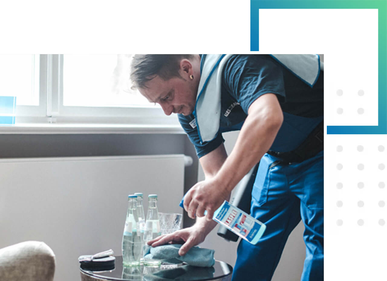 Gesundheit und Hygiene liegen uns am Herzen. Ein Mitarbeiter in Arbeitskleidung desinfiziert einen kleinen Tisch in einem Kundenwartebereich. Hygiene liegt uns am Herzen.